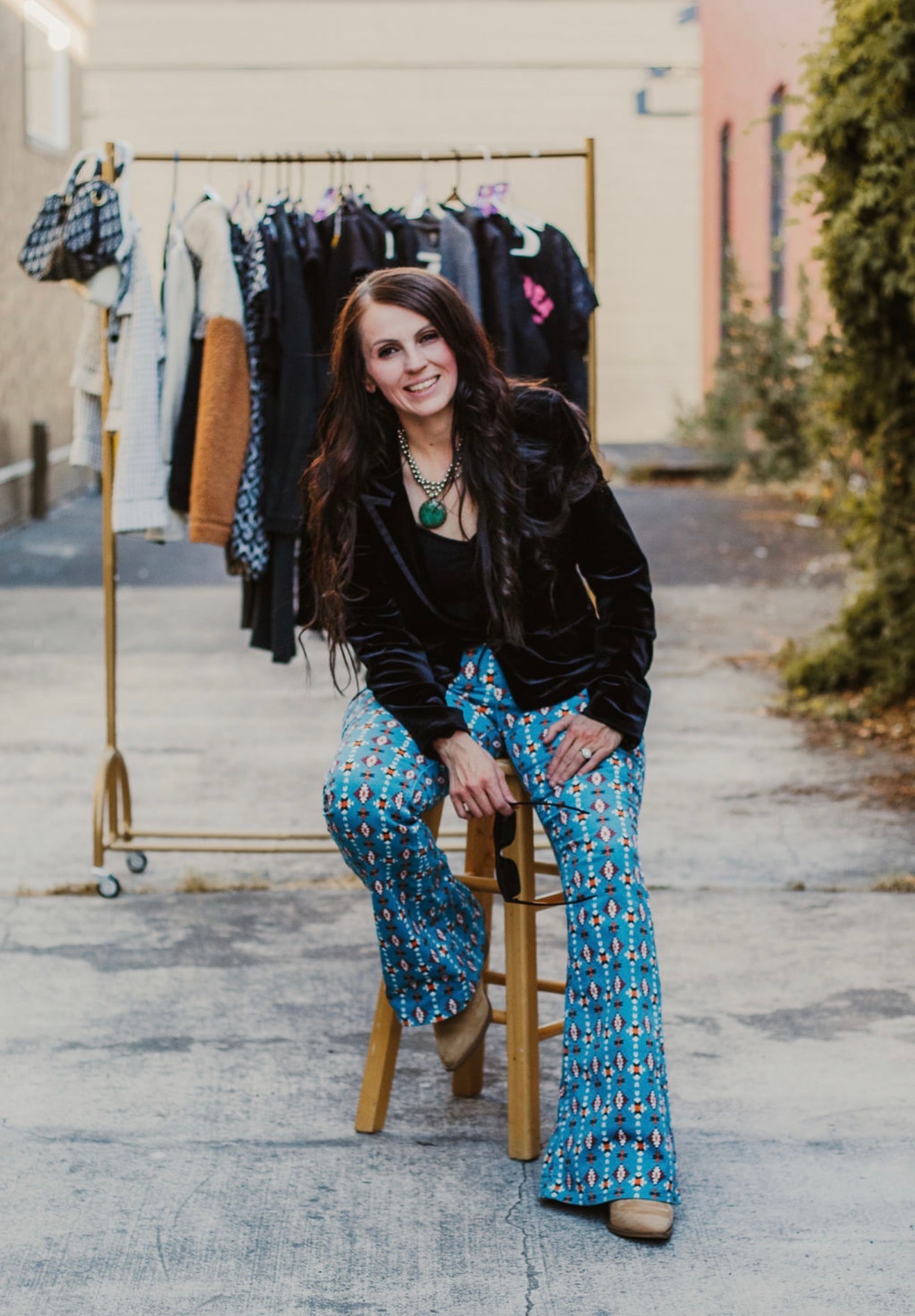 Brittney Holladay seated on a stool in front of a rack of hand-picked clothing
